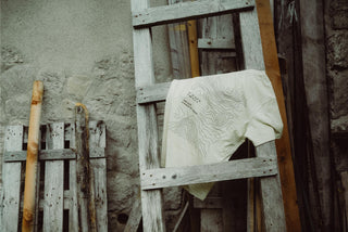 Das Origin T-Shirt in Beige auf einer Holzleiter einer Alm. Weil wir die Natur lieben.