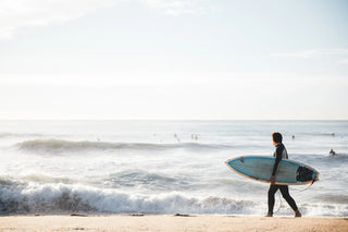 Surfer mit Surfboard am Strand bei guten Wellen am Meer. Surferlook und coole Kleidung für den Sommer online kaufen.